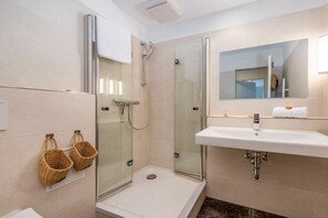 Un baño moderno con ducha envuelta en vidrio, un lavamanos blanco y dos cestas de mimbre en la pared.
