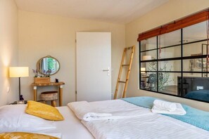 Een hotelkamer met twee bedden, een spiegel, een raam met uitzicht, een ladder en een lamp.