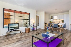 Una sala de estar moderna con un televisor de pantalla plana, una mesa de centro de vidrio y un comedor con mesa y sillas.
