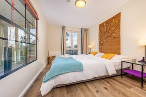 Un dormitorio con cama, ventana, lámpara de pared y vistas al exterior.