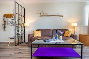 Un salon moderne avec une table basse en verre, un canapé marron et une cloison en verre agrémentée de plantes.