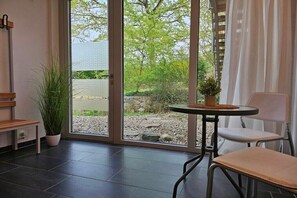 Een kamer met een schuifdeur naar een tuin, een kleine ronde tafel met een plant en een witte stoel.
