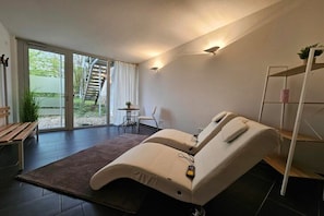 Une pièce moderne équipée d’une table de massage, d’un banc, d’une petite table avec une plante et d’un escalier menant à l’extérieur.