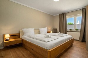 Um quarto com cama de madeira, duas mesas de cabeceira com luminárias, uma janela com cortinas e vista para o verde lá fora.