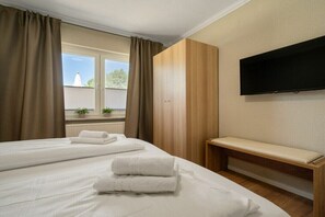Een hotelkamer met twee bedden, een bankje, een televisie en een raam met gordijnen.