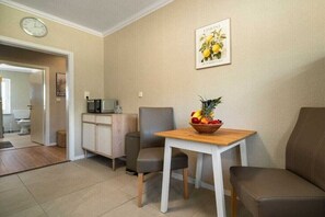 Un pequeño espacio de estar con una mesa de comedor, dos sillas, un microondas y un reloj en la pared.