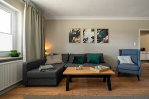 Een woonkamer met een bank, een bijzettafeltje en een stoel. Er hangen drie schilderijen aan de muur.