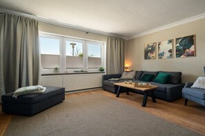 Een woonkamer met een bank, een salontafel, een raam met gordijnen en wanddecoratie.