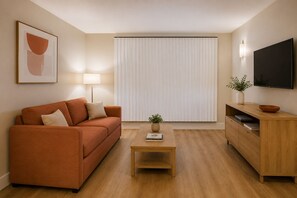 A modern living room with a sofa, a coffee table, a TV, and a window with blinds. - The Vionelle Hotel (Toronto)
