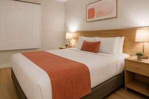 A neatly made bed with a brown throw, two bedside tables with lamps, a wooden headboard, and a framed abstract painting on the wall. - The Vionelle Hotel (Toronto)
