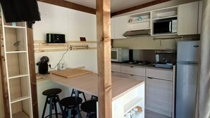Cocina compacta con techo de vigas de madera, microondas, estufa, refrigerador y una pequeña barra con taburetes.