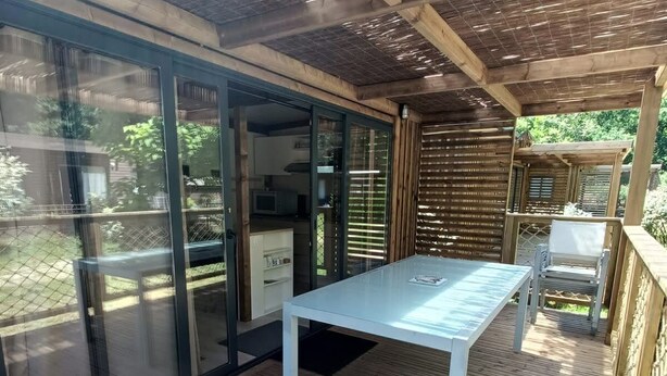 Un patio techado al aire libre con una mesa y sillas, una puerta corrediza de vidrio que da a una zona de cocina y una terraza de madera.