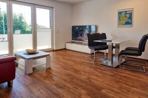 A modern living room with a TV, a dining table, and chairs. - Holiday apartment with 1 bedroom (Sassnitz)