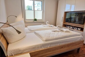 Ett sovrum med två sängar, en TV och ett fönster med persienner.