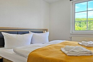 Une chambre d’hôtel avec un lit, du linge de lit blanc, une fenêtre donnant sur un paysage verdoyant et un radiateur.