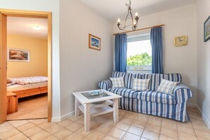 Une pièce comprenant un lit, un canapé, une petite table, une fenêtre avec des rideaux, une horloge murale et un tableau.