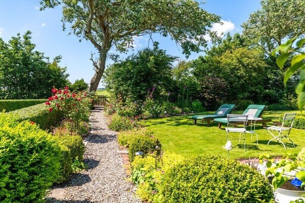 Un jardin avec un chemin de gravier, des chaises vertes et une variété de plantes.