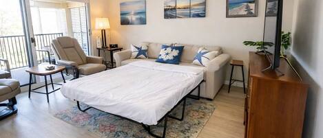 Un dormitorio con cama, sofá, sillón, mesita, lámpara y obras de arte en las paredes.