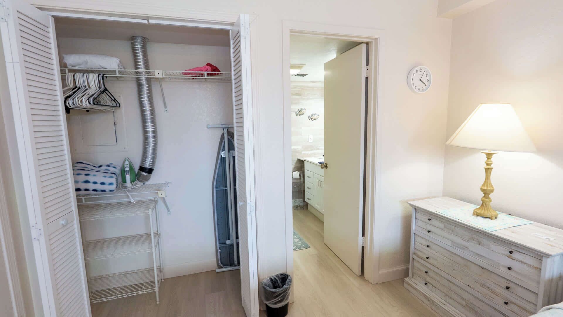 Hotellihuone, jossa on erillinen vaatehuone, kylpyhuone suihkulla sekä yöpöytä lampulla.