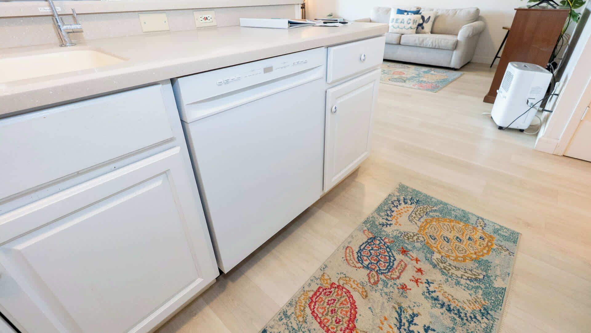 Una cocina con gabinetes blancos, lavavajillas y un tapete estampado en el suelo.