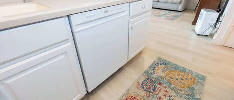 Una cocina con gabinetes blancos, lavavajillas y un tapete estampado en el suelo.