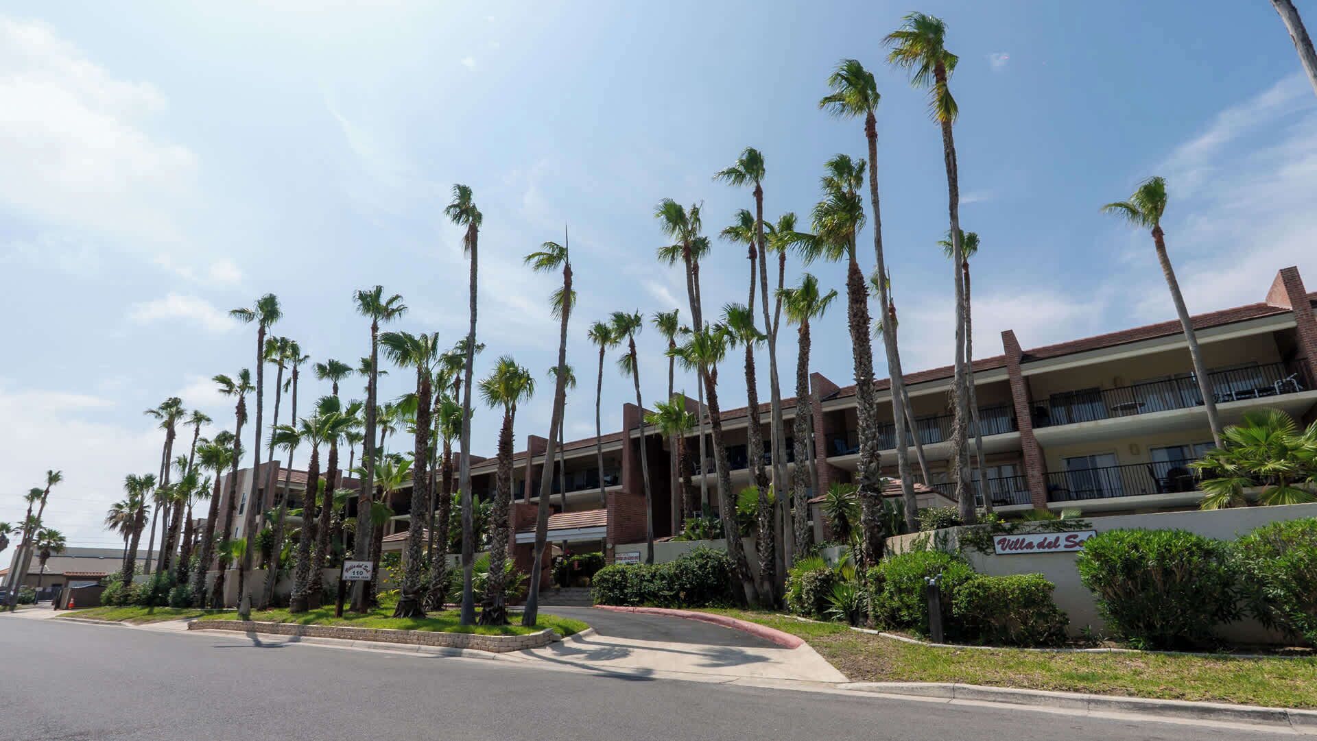 A hotel with multiple floors, palm trees, and a clear sky.