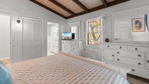 Ein Schlafzimmer mit Bett, Schminktisch, Fernseher und einem Fenster mit Jalousien.