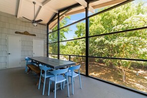 Zona pranzo con tavolo e sedie, ampie finestre e ventilatore a soffitto.