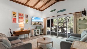 Ein Wohnzimmer mit Holzboden, einem Essbereich mit Tisch und Stühlen, einem Sofa, einem Schrank und einem großen Fenster mit Blick ins Freie.