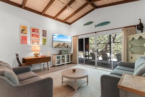 A living room with a wooden ceiling, a dining area with a table and chairs, a sofa, a cabinet, and a large window with a view of the outdoors. - Family Beach Escape 5BR Fenced Yard, Walk to Ocean (Pawleys Island)
