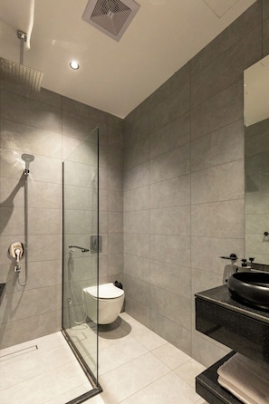 Un baño moderno con cabina de ducha de vidrio, inodoro blanco y lavamanos negro con espejo superior.