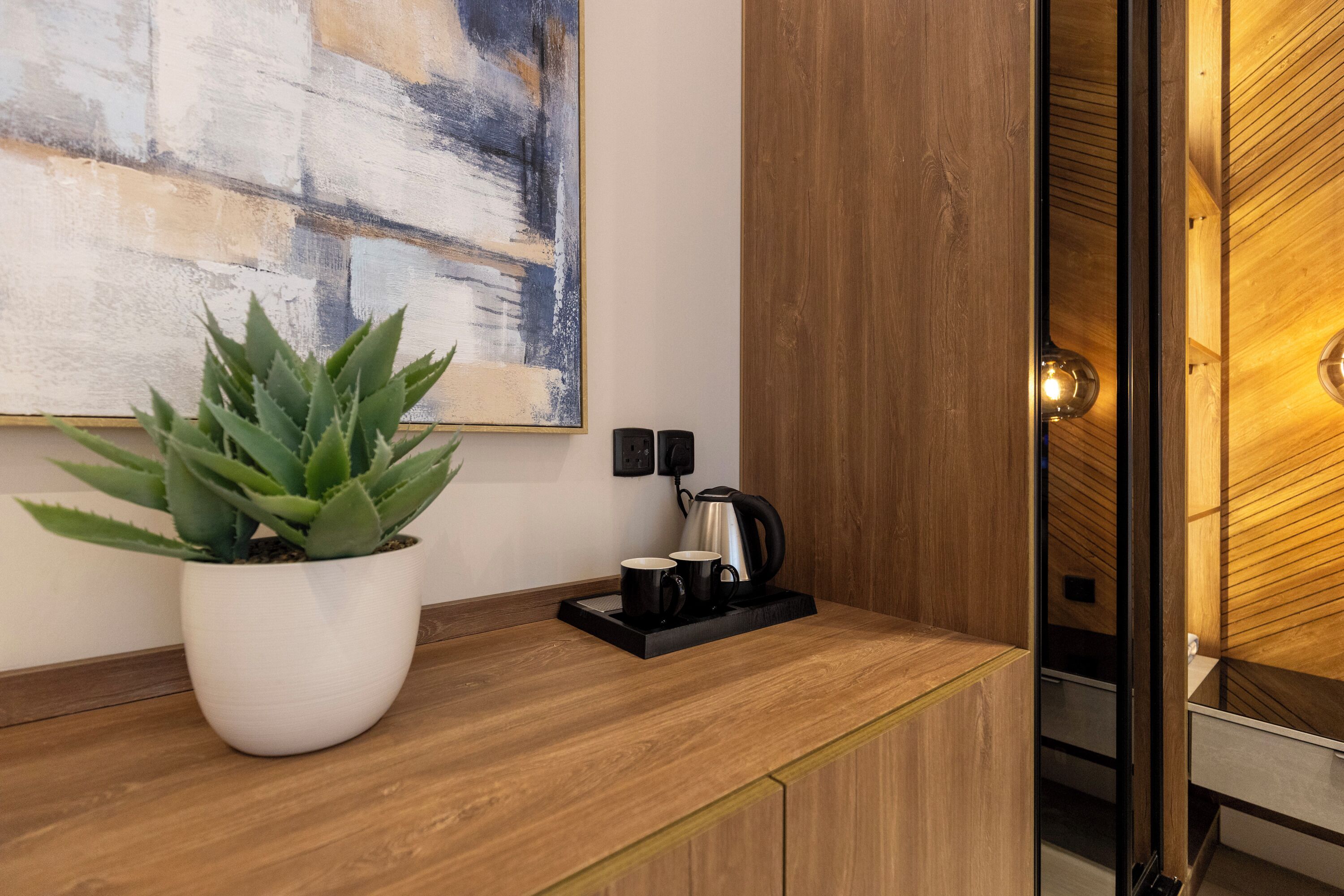 Une cuisine moderne avec un plan de travail en bois, une plante en pot, une machine à café et un tableau accroché au mur.