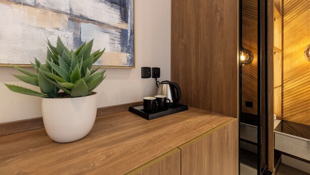 A modern kitchen with a wooden countertop, a potted plant, a coffee maker, and a painting on the wall. - Elegant Studio Near Quba Mosque Prime Location (Madinah)