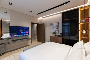 A modern hotel room with a large bed, a flat-screen TV mounted on the wall, a wooden cabinet, and a sliding door closet. - Elegant Studio Near Quba Mosque Prime Location (Madinah)