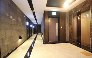 A modern hallway with a marble floor, dark walls, and a glass elevator. - MU Plus Hotel Busan (Busan)