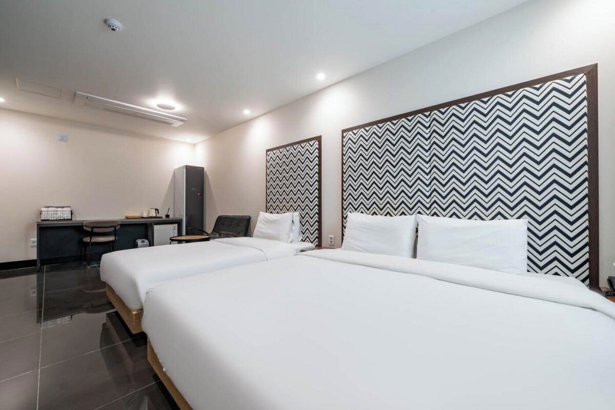 Habitación de hotel con dos camas, un escritorio, una silla y un armario.