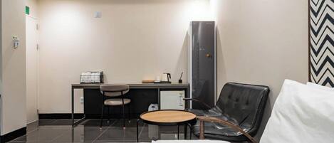 Una habitación de hotel con una cama, un escritorio con una silla, una mesita y un refrigerador.