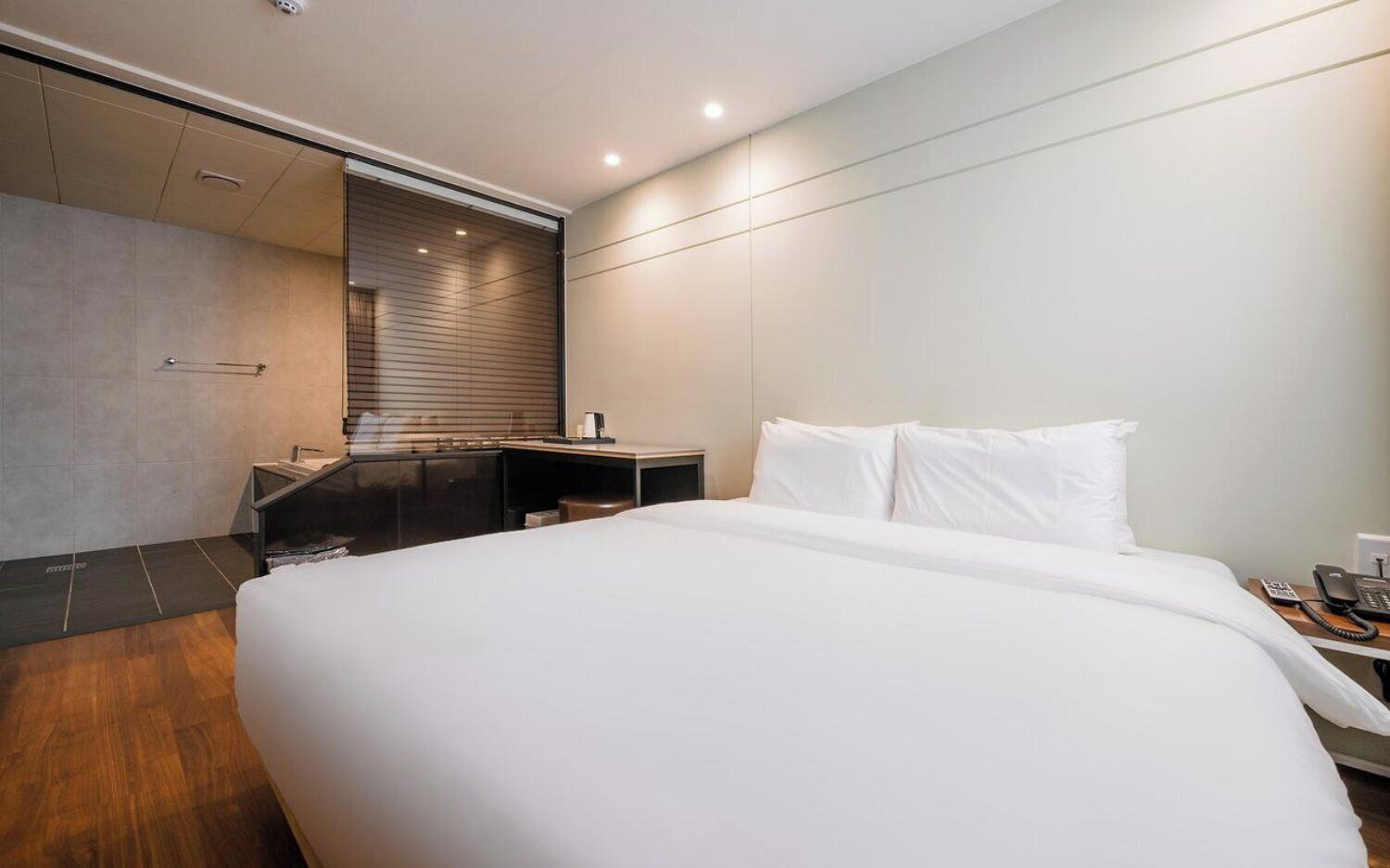 Habitación de hotel moderna con una cama grande, un escritorio, zona de ducha y vistas a la ciudad.