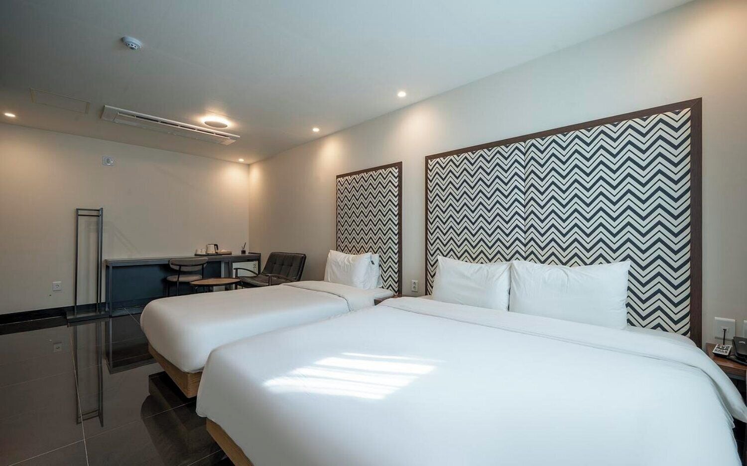 Quarto de hotel com duas camas, uma escrivaninha e uma cadeira.