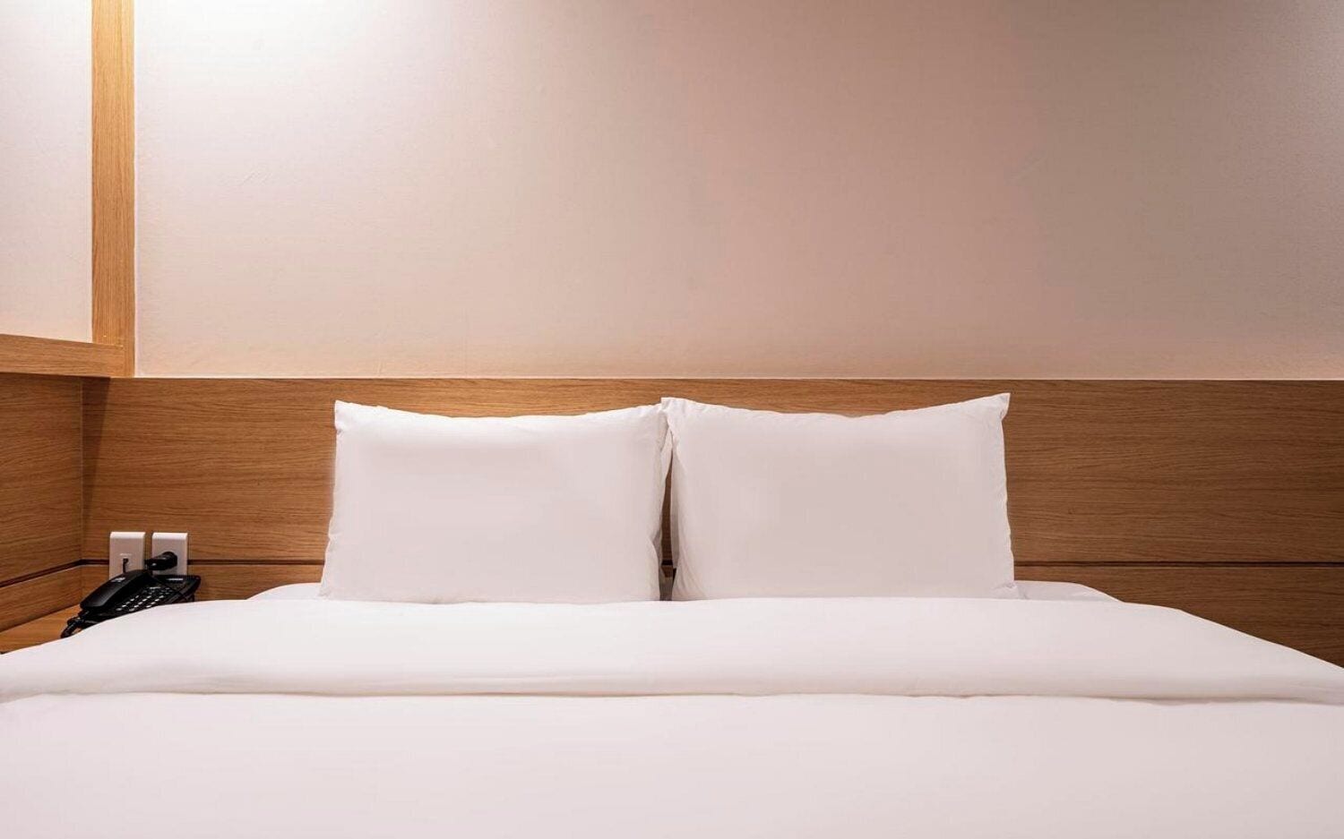 A hotel room with a wooden headboard, a bed with white linens, and a telephone on the side.