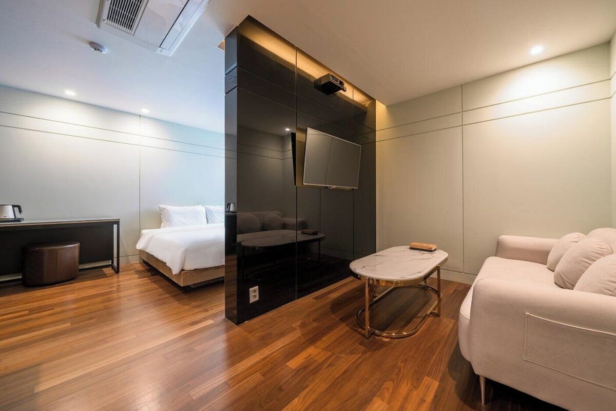 Una habitación de hotel moderna con cama, sofá, una mesita y televisor.