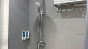 A shower with a handheld showerhead, a wall-mounted faucet, and a towel rack with towels.