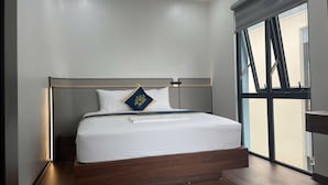 A modern hotel room with a large bed, a headboard, a window with blinds, and an air conditioning unit. - HD Villa Hotel An Quy - by BAY LUXURY (Hanoi)
