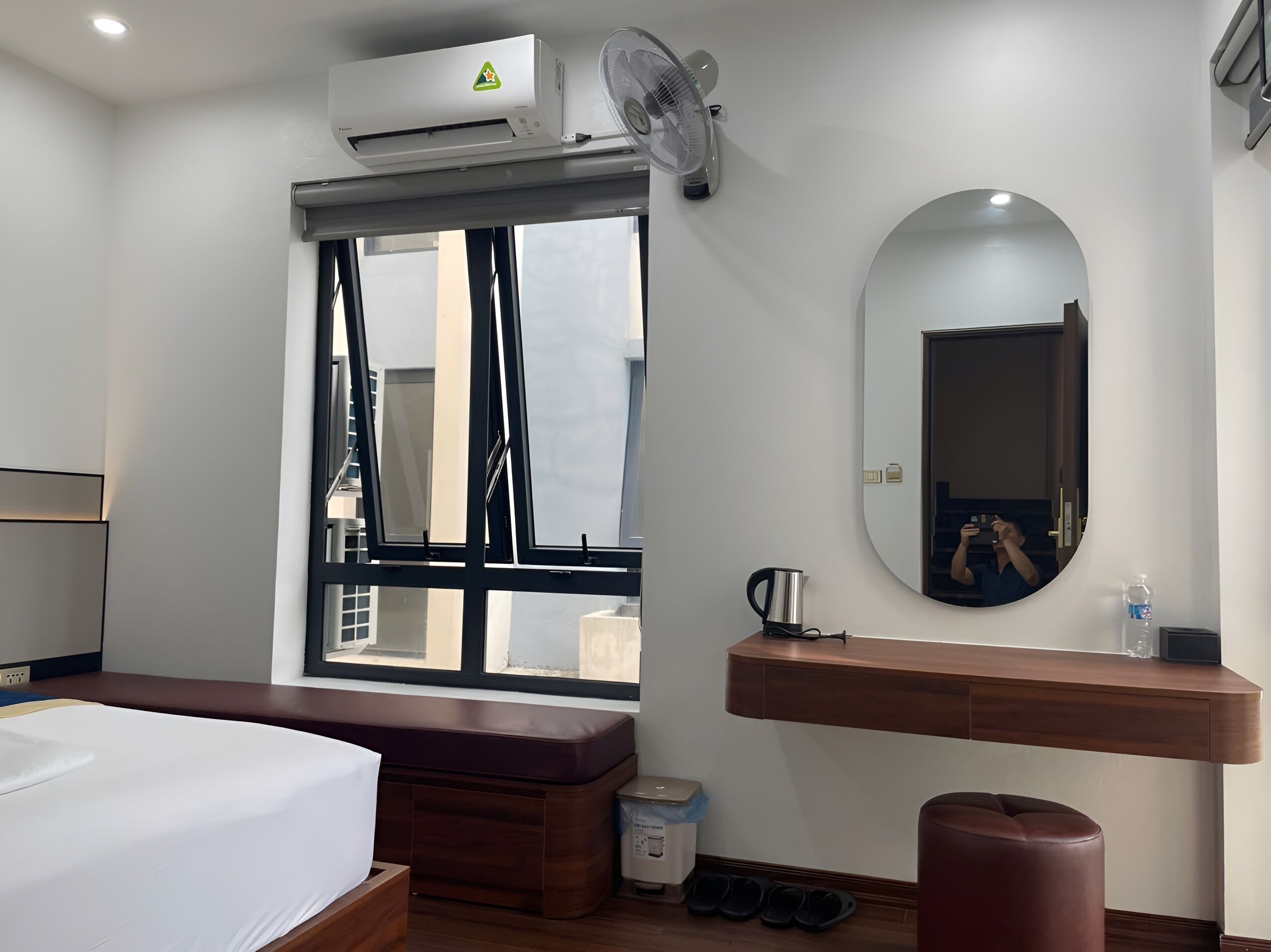 Ein Hotelzimmer mit Bett, Fenster, Spiegel, Nachttisch mit Wasserkocher und einem kleinen Hocker.