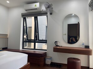 Ein Hotelzimmer mit Bett, Fenster, Spiegel, Nachttisch mit Wasserkocher und einem kleinen Hocker.