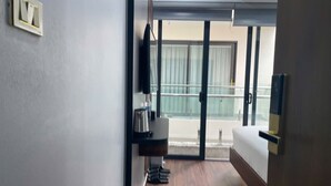 A hotel room with a bed, a small desk with a chair, a TV mounted on the wall, and a balcony with a view.