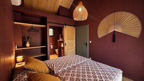 A bedroom with a bed, bedside tables, a hanging light fixture, and a wall-mounted fan.
