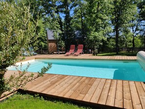 A swimming pool with wooden deck and red lounge chairs.