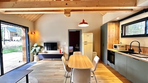A modern kitchen with a dining area, wooden ceiling beams, a TV, and a view of the outdoors.