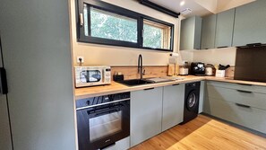 A compact kitchen with a built-in oven, a dishwasher, a sink, and a window above the countertop. - Maison bois avec piscine au cœur du Périgord Noir (Nadaillac)